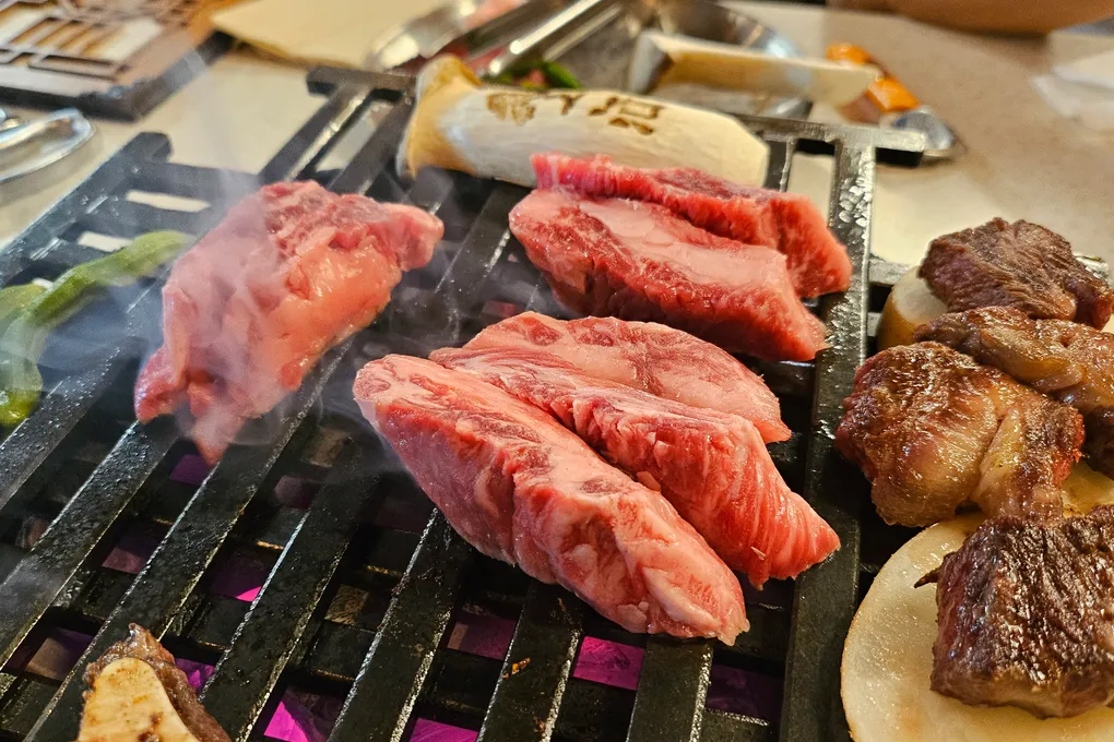 Hanwoo beef and shishito peppers grilling on a cast-iron charcoal plate at Baeksong