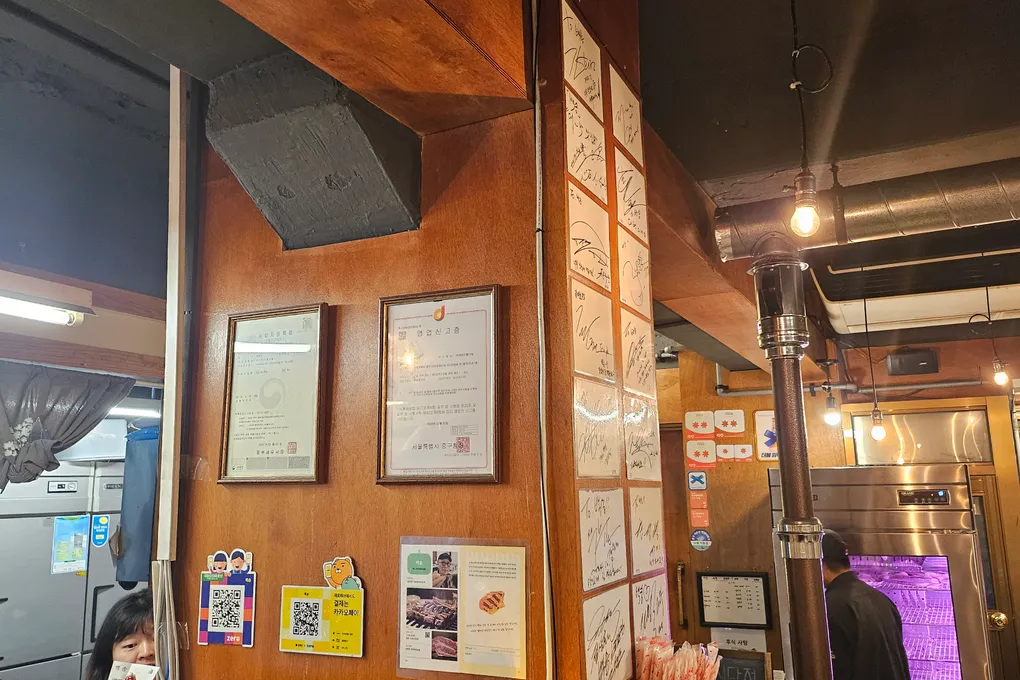 Interior of Baeksong with wooden walls, framed certificates, hanging lights, and a beef display fridge