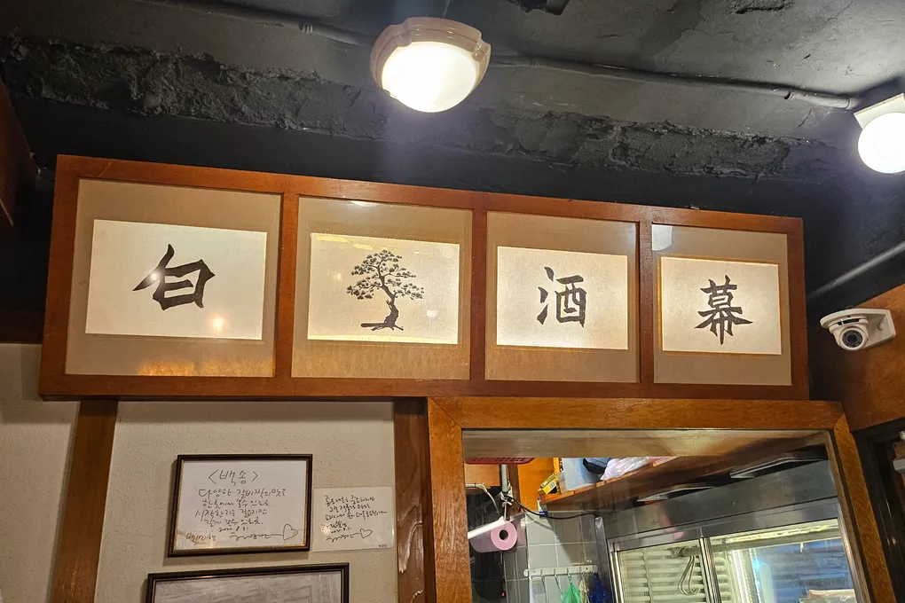 Framed calligraphy and a pine-tree painting on the wall at Baeksong
