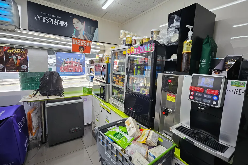 The counter area of a Korean convenience store with a coffee machine, hot food case, and microwave zone