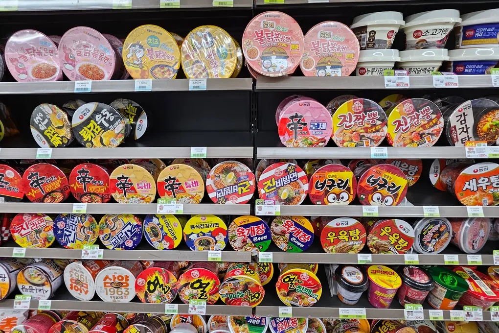 Shelves of cup ramen at a Korean convenience store including Shin Ramyun and Yukgaejang