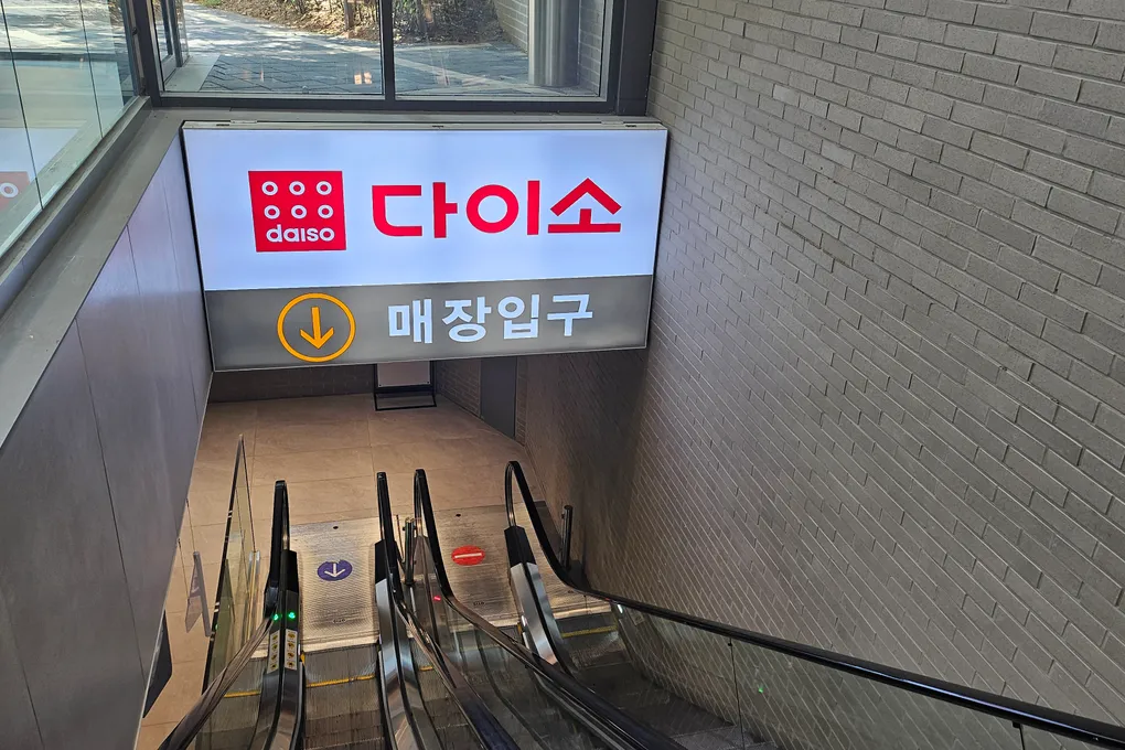 The entrance to a Daiso store in Seoul with the red Daiso sign and an escalator going down