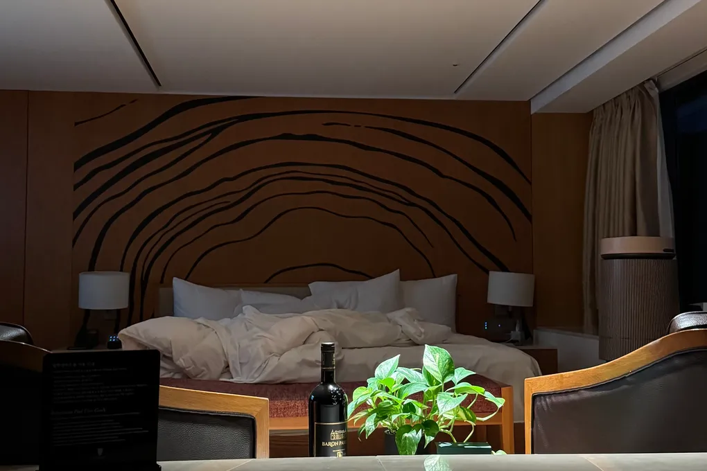 Guest room bed at Banyan Tree Club & Spa Seoul with a wood-grain headboard wall and a welcome bottle of wine