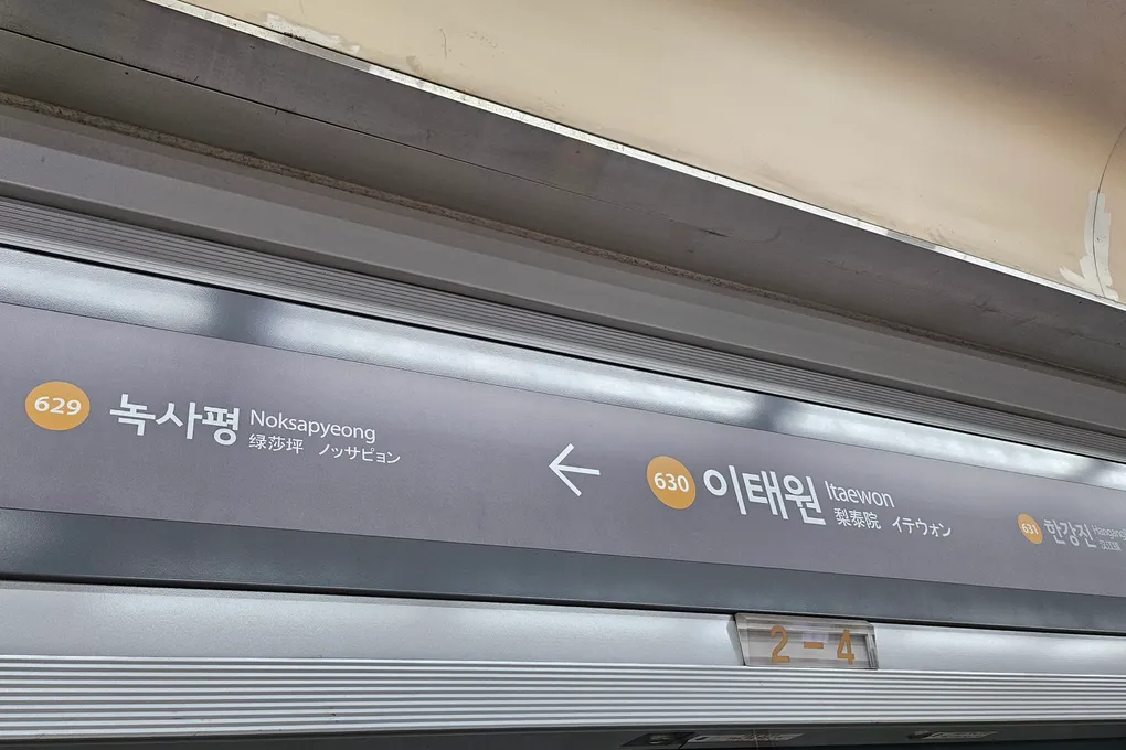 A hand tapping a transit card on the reader at a Seoul subway fare gate, showing the balance