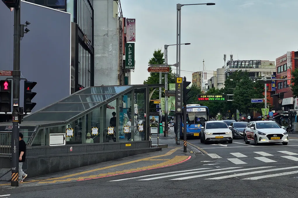 Street view coming out of an Itaewon Station exit, with shops, buses and a crossing