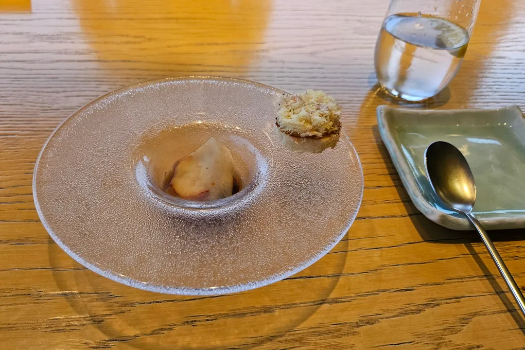 A textured clear glass plate holding a pale poached item in a shallow well, with a small crumb-topped bite on the rim