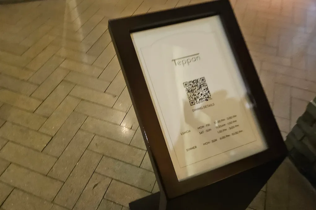 A framed standing sign at the entrance to Teppan showing a QR code and dining hours for lunch and dinner